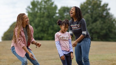 Three people of diverse ages and backgrounds enjoy time outside together in a tree-lined city park.