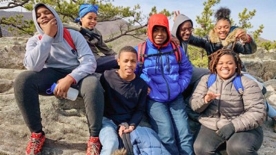 A group of seven kids sitting on large rocks pose for the camera